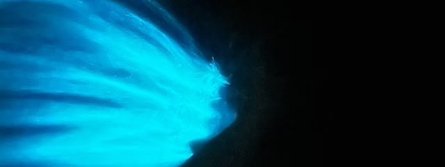 Blue-green bioluminescent light glowing in the ocean at night